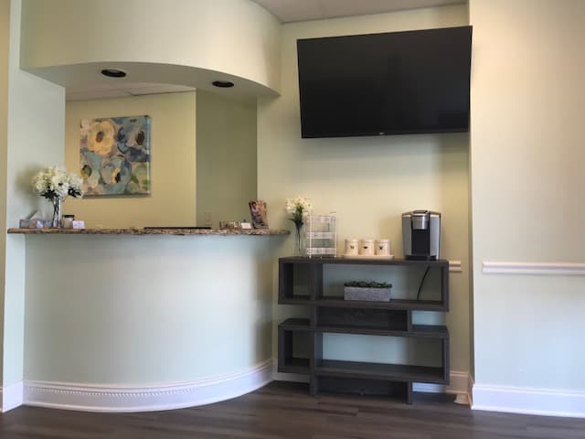 Reception area at Matlock Family Dental with a curved granite-topped front desk, fresh flowers, wall-mounted television and a coffee station